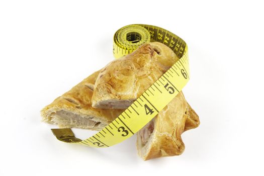 Single golden sausage roll cut in half with pork pie and yellow tape measure on a reflective white background