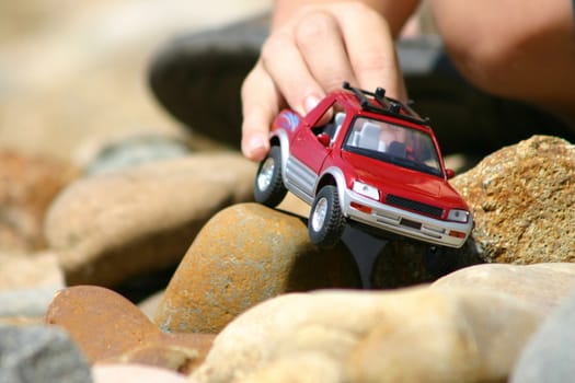 Child playing with a toy car in a stoney area.