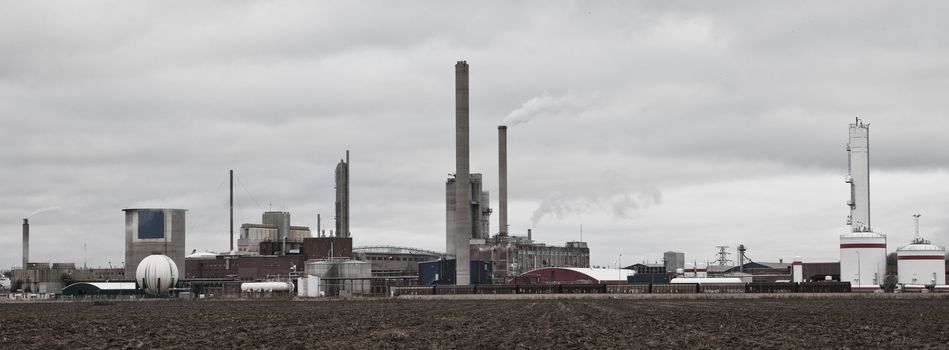 Industrial buildings behind a field on a cloudy day