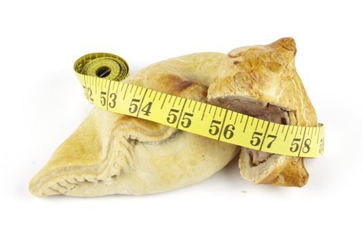 Single golden pasty with pork pie and yellow tape measure on a reflective white background