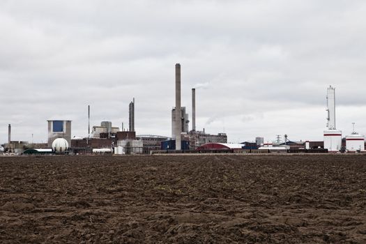 Industrial buildings behind a field on a cloudy day