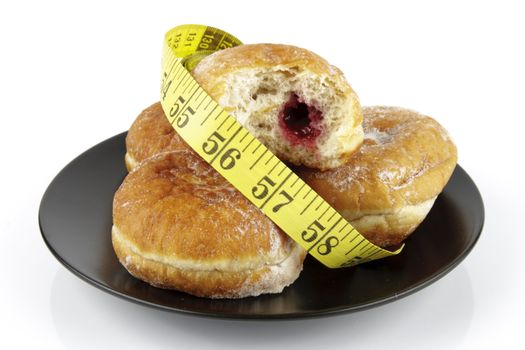 Black round plate of jam doughnuts with a yellow tape measure on a reflective white background