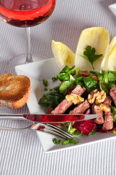 mixed salad on a white plate with a glass of rose