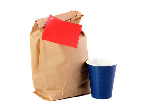 Paper package for a dinner of the schoolboy, the student, the employee or the worker, on a package a red piece of paper for the message and nearby a paper cup for water.