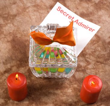 A note from a secret admirer is placed inside a candy dish beside two burning candles