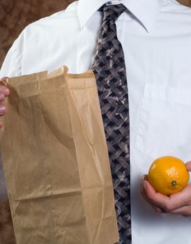 Closeup businessman showing off his healthy lunch featuring a paper bag and a fresh orange