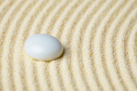 Round ceramic stone on a surface of yellow sand close up