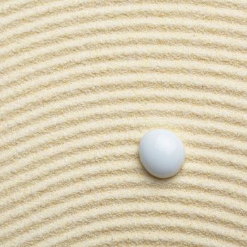 Round ceramic stone on a surface of yellow sand - square composition