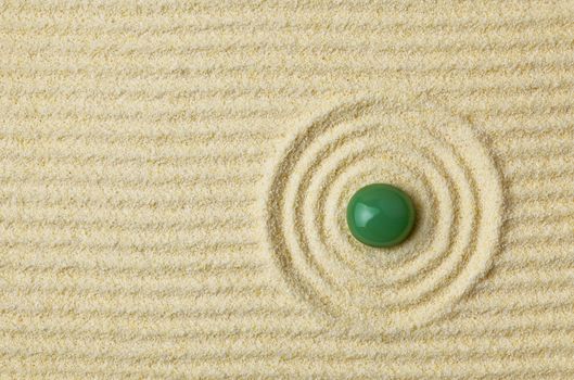 Round green stone on a surface of yellow sand