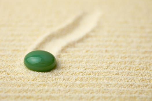 Round green stone on a surface of yellow sand