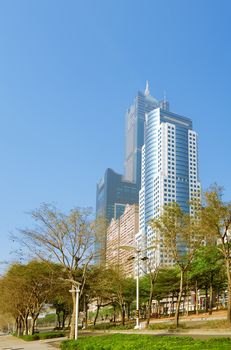 Skyscraper on the street with blue sky and green tree in modern city.