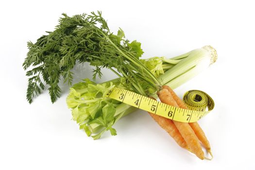 Fresh bunch of orange carrots with green leafs and celery with a yellow tape measure on a reflective white background