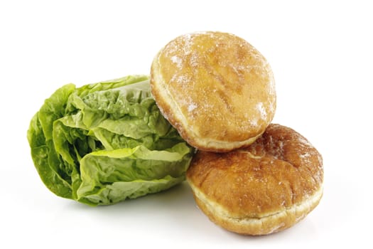 Contradiction between healthy food and junk food using a green salad lettace and jam doughnut on a reflective white background 