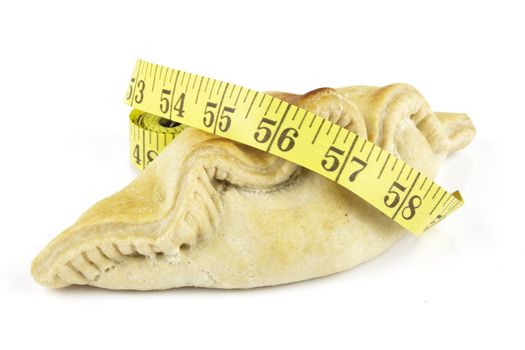 Single golden pasty and yellow tape measure on a reflective white background