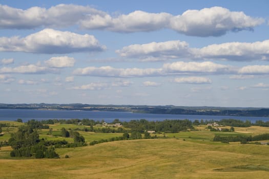 Landscape of fields and lake with clouds, captured in Latvia