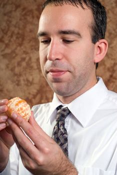 A young businessman wearing a white shirt and tie is holding a peeled orange