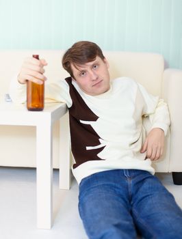 Drunken man sits on a floor with a beer bottle in a hand