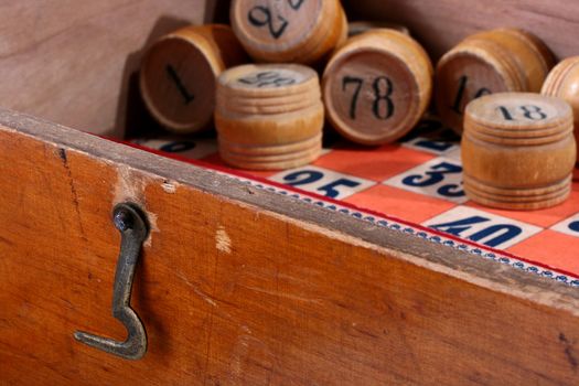 Ancient game of a lotto, analogue bingo. In a box kegs with figures and game cards lie. In the foreground a hook closing a box cover.