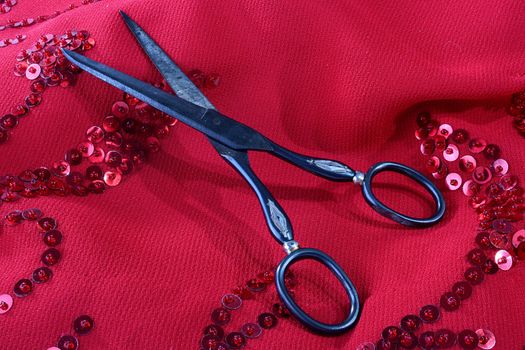 Red fabric embroidered by beads, in the foreground ancient scissors.