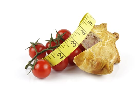 Contradiction between healthy food and junk food using tomatoes and a pork pie with a tape measure on a reflective white background 