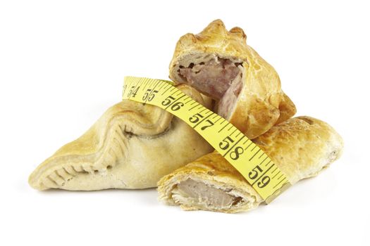 Single golden sausage roll cut in half with pork pie and pasty with a yellow tape measure on a reflective white background