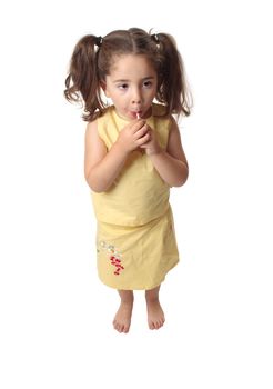 A small preschool girl eating a sweet lollipop.  She is barefoot and wearing a skirt and top with hair in ponytails.