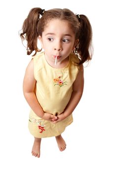 A small cute girl with hair in ponytails is sucking on a lollipop sweet.   She is standing on a white background and looking sideways.  Space for copy.