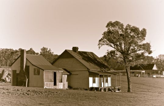 an old house of a cattle station or ranch in the middle of the field in sepia