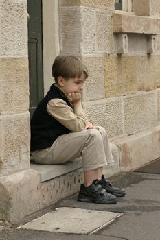 Young boy sitting on the doorstep. Feeling a little glum 

eg: glum, lonesome, outcast, troubled, grief, ponder 
