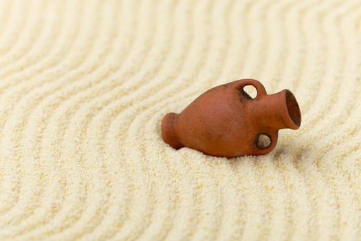 The ancient clay amphora lies on a surface of yellow sand