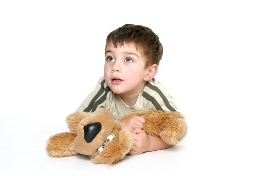 Child dressed in casual clothes,  laying on the floor holds closely a plush toy dog.  He is looking up, space for text.