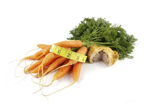 Contradiction between healthy food and junk food using bunch of carrots and pork pie with a tape measure on a reflective white background 