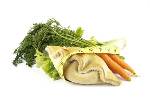 Contradiction between healthy food and junk food using a bunch of carrots and pasty with a tape measure on a reflective white background 