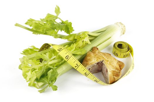 Contradiction between healthy food and junk food using celery and pork pie with a tape measure on a reflective white background 