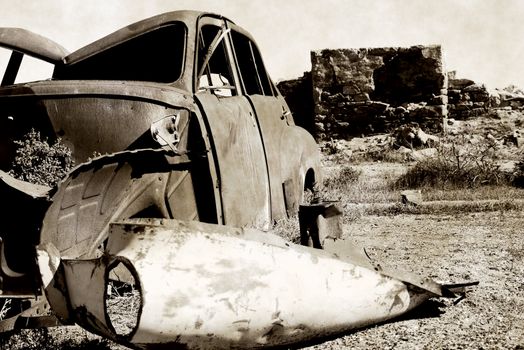 black and white image an old rusting car and ruins in the desert