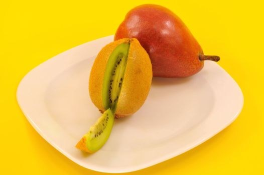 kiwi  sliced and pear on a white plate on a yellow background 
