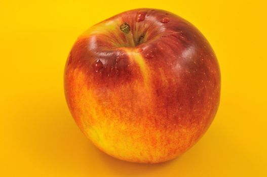 
red appetizing apple with drops of water on a yellow background