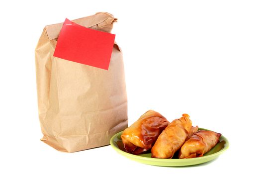 Paper package for a dinner at office or at school and pancakes with a stuffing on a plate.