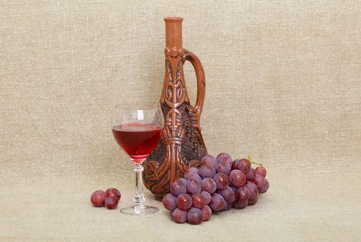 Composition from clay Georgian bottle, a glass and grapes against old canvas
