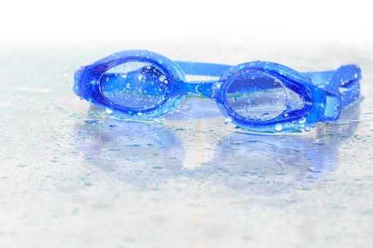 Blue wet swimming goggles on glass background with water drops