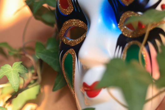 Closeup of nice ceramic venetian mask on background with green leaves