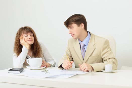 The woman falls asleep sitting at a table with a huge cup of coffee