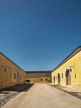 Big yellow house with an empty  alley in France under pure blue sky