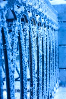 Close up view of frozen black iron fence and big frost on it. Blue colours.