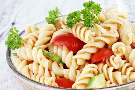 Pasta salad with dressing, fresh tomatoes, cucumbers and parsley. Shallow depth of field.

