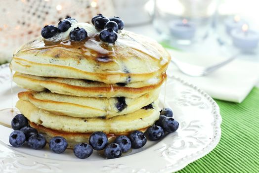 Stack of fresh pancakes dripping with butter and maple syrup. Garnished with fresh blueberries.

