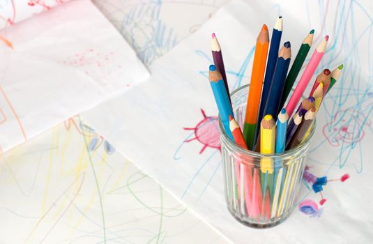 Colored pencils in a glass on a child's drawing