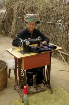 Femme ethnie Hmong noir devant sa machine à coudre .Elle est installée devant sa maison .Ses mains sont bleues de la teinture du tissus qu’elle coud .Cette machine est l’unique fortune du couple .