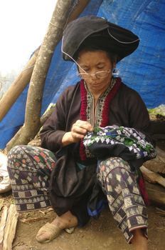 Femme ethnie Dao noir  brodant un pantalon .Les motifs sont rituels et la technique est toujours la même depuis des siècles