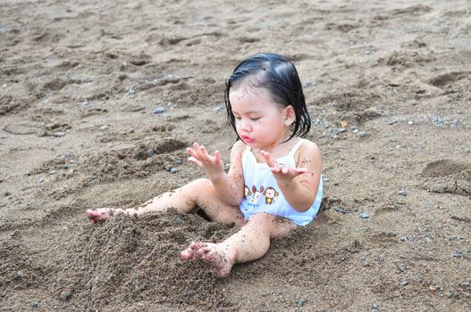 Cute little girl playing with sand for the first time at the beach.